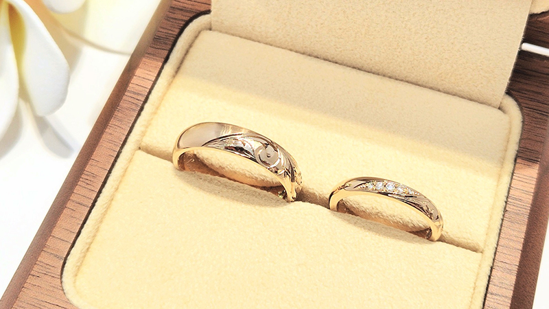 おふたりがお選びされた地金の素材は、肌馴染みがよく、深みがあり大人の品格を感じさせる「ブラウンゴールド」です。
 
手彫りのデザインはお揃いで、”永遠に受け継がれる想い”という意味合いの波のデザイン「ヘリテイジ」をお選びいただきました。
また、手彫り部分の表面加工としてお選び頂いた波のアウトライン外側に砂模様を施す「サンドアウト」が、波のデザインをより立体的に浮き上がるような存在感のある雰囲気に演出してくれます。
