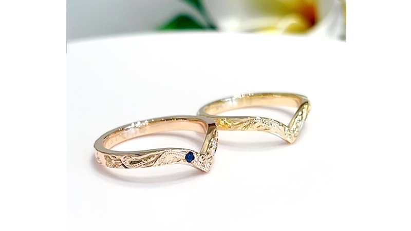 ハワイ伝統の手彫りのデザインは、2種類のデザインを半周毎楽しめる特別仕様のハーフデザインに。
&nbsp;
正面のメインのデザインは、波をモチーフにした”永遠に受け継がれる想い”という意味が込められた「ヘリテイジ」に、ポイントとして 「プルメリア」のお花を中心と両サイドのデザイン切り替え部分にひとつずつ配置されました。
&nbsp;
更に、波の表面加工としてアウトラインに沿ってジグザグの「リーグル」の装飾彫りを施され、より華やかな雰囲気に。
「リーグル」は、昔は王族のみが身に着けることが許されており、現代では富や豊かさをもたらしてくれるとされています。
